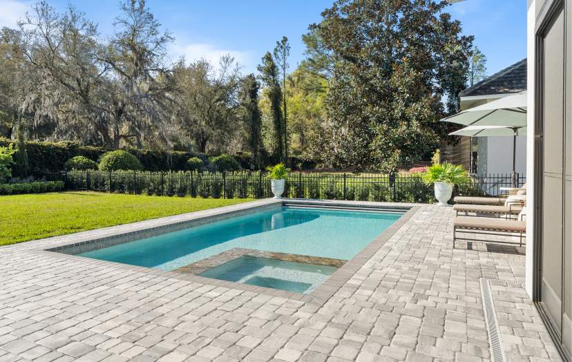 A grey brick patio featuring a swimming pool and green landscape