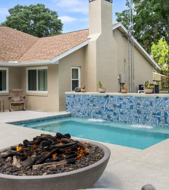 A pool area with a waterfall surrounded by a patio with a firepit