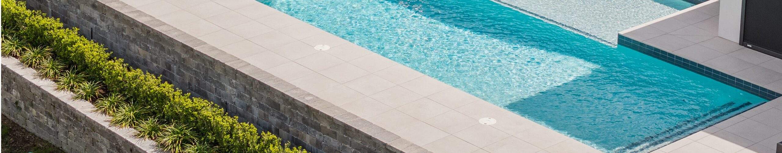 A pool with surrounded by a retaining wall and greenery
